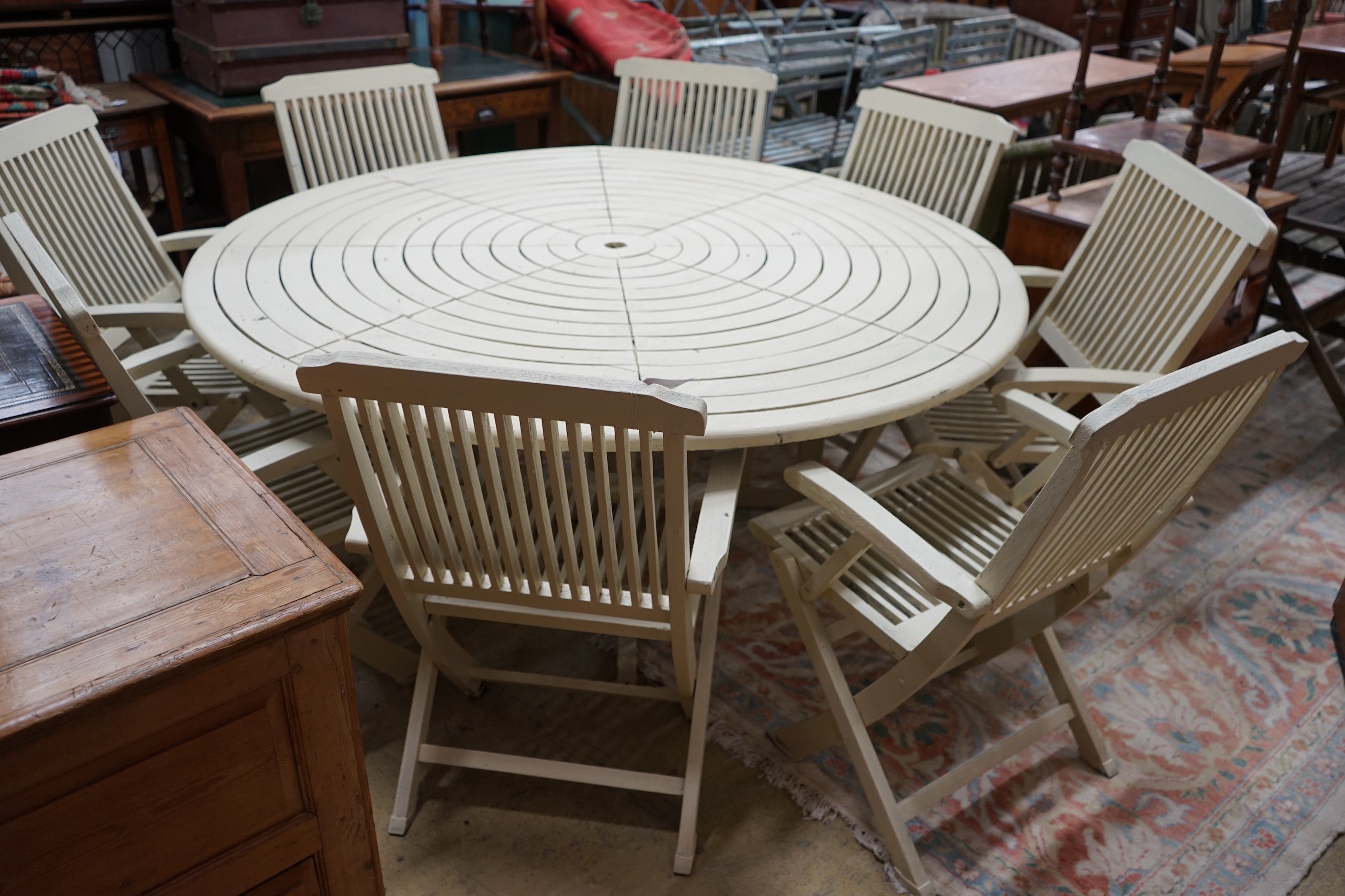 A circular painted teak garden table, diameter 180cm, height 72cm and eight matching folding garden elbow chairs
